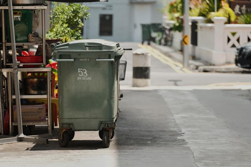 Green garbage cart on a quiet street in sunlight