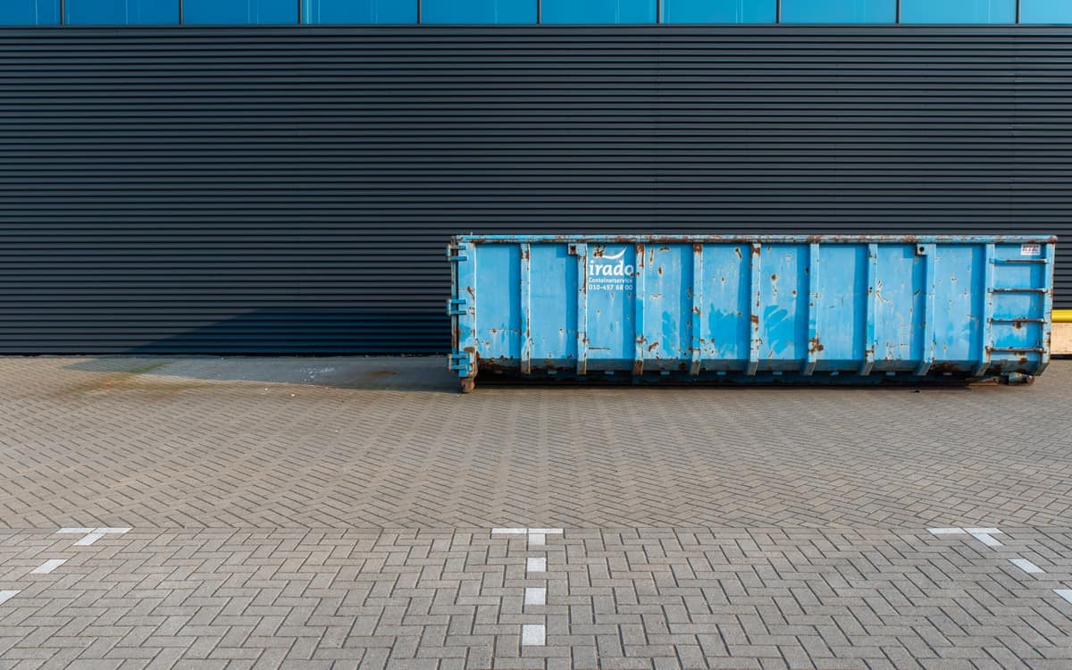 Blue commercial dumpster beside a modern building